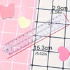 Regla plegable de acrílico transparente junto a recortes en forma de corazón rosa, mostrando su tamaño y marcas.
