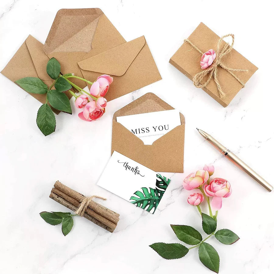 Eine Sammlung von Kraftpapier-Umschlägen mit Schnur, rosa Rosen und grünen Blättern.