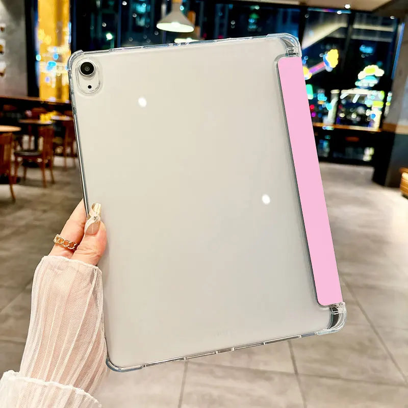 A hand holds a clear anti-drop tablet case for an iPad with a pink protective cover in a dimly lit indoor setting.