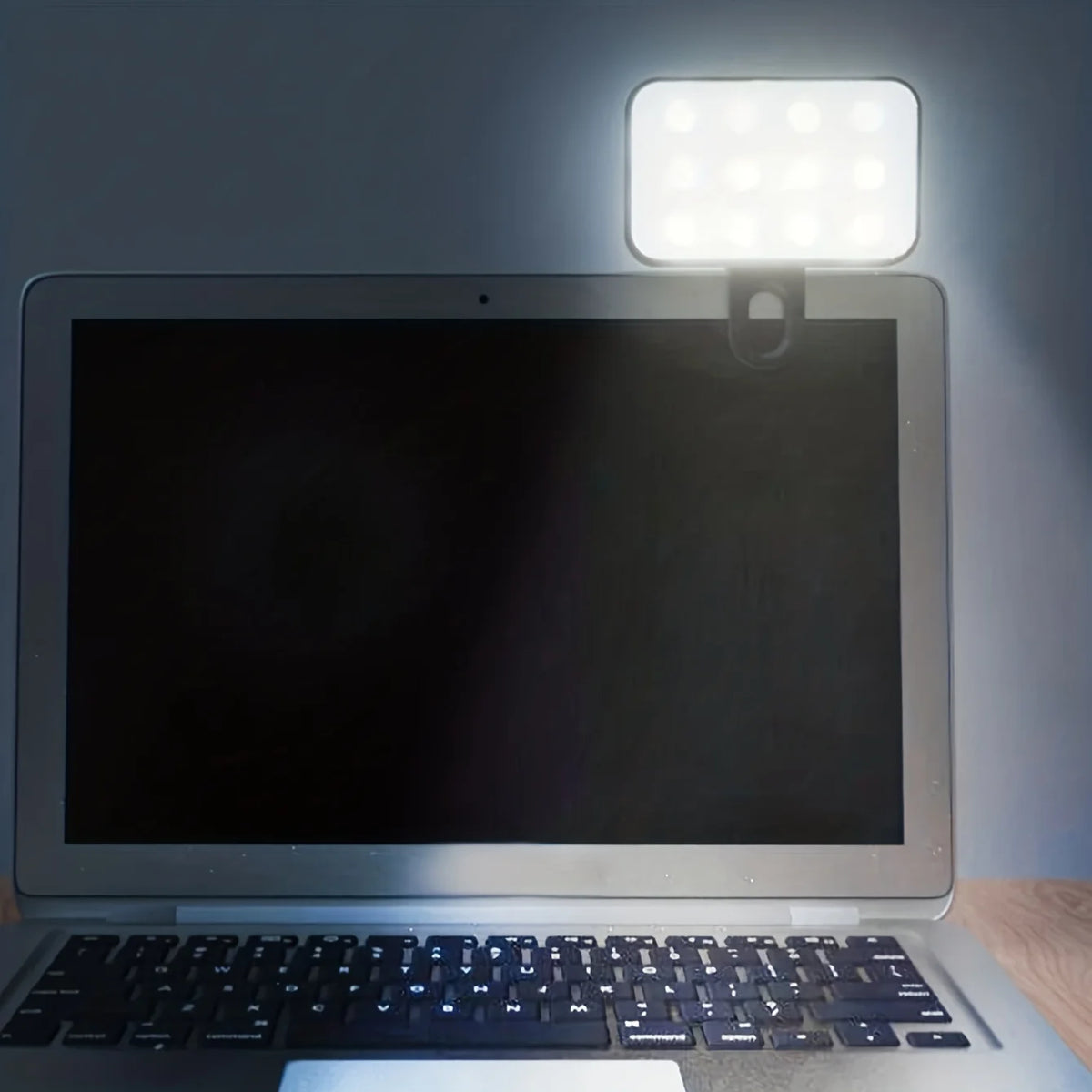 A laptop is illuminated by a portable rechargeable mini selfie light positioned above the screen.