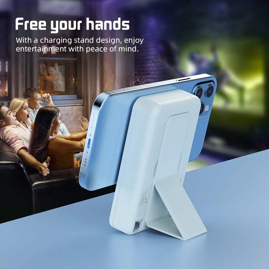 A light blue portable magnetic wireless power bank is shown resting on a table, with people in the background enjoying entert
