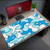 A blue and white wave pattern mouse pad placed on a wooden desk next to a computer monitor.