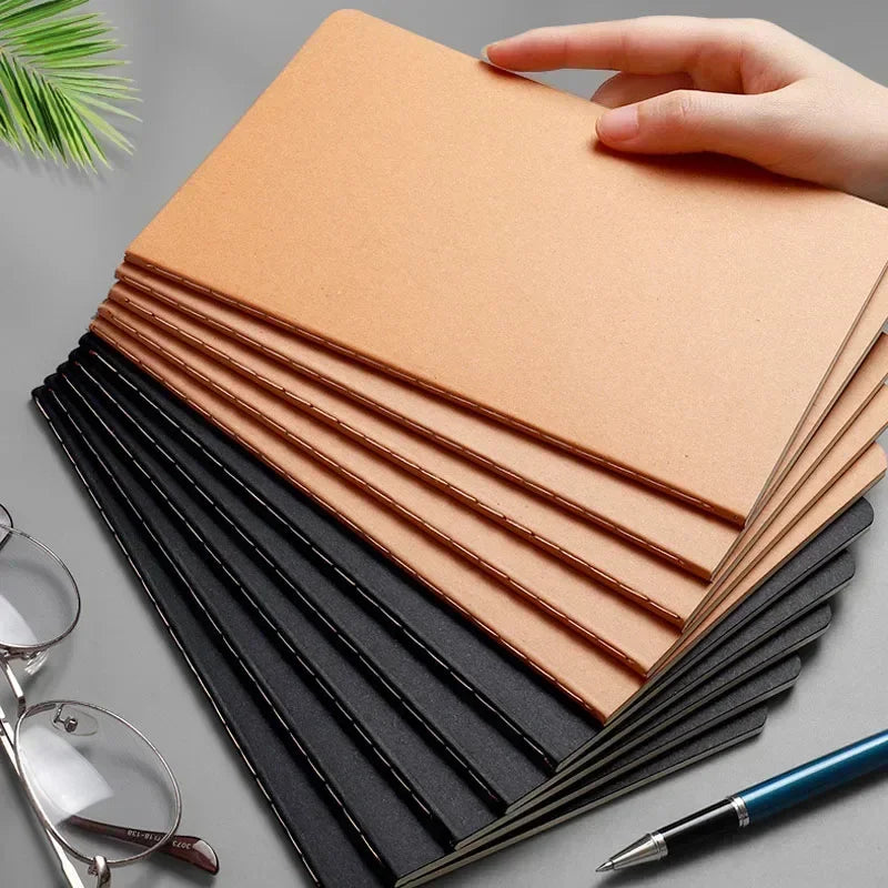 A stack of A5 Kraft cover notebooks in brown and black are shown next to a pair of glasses and a pen.