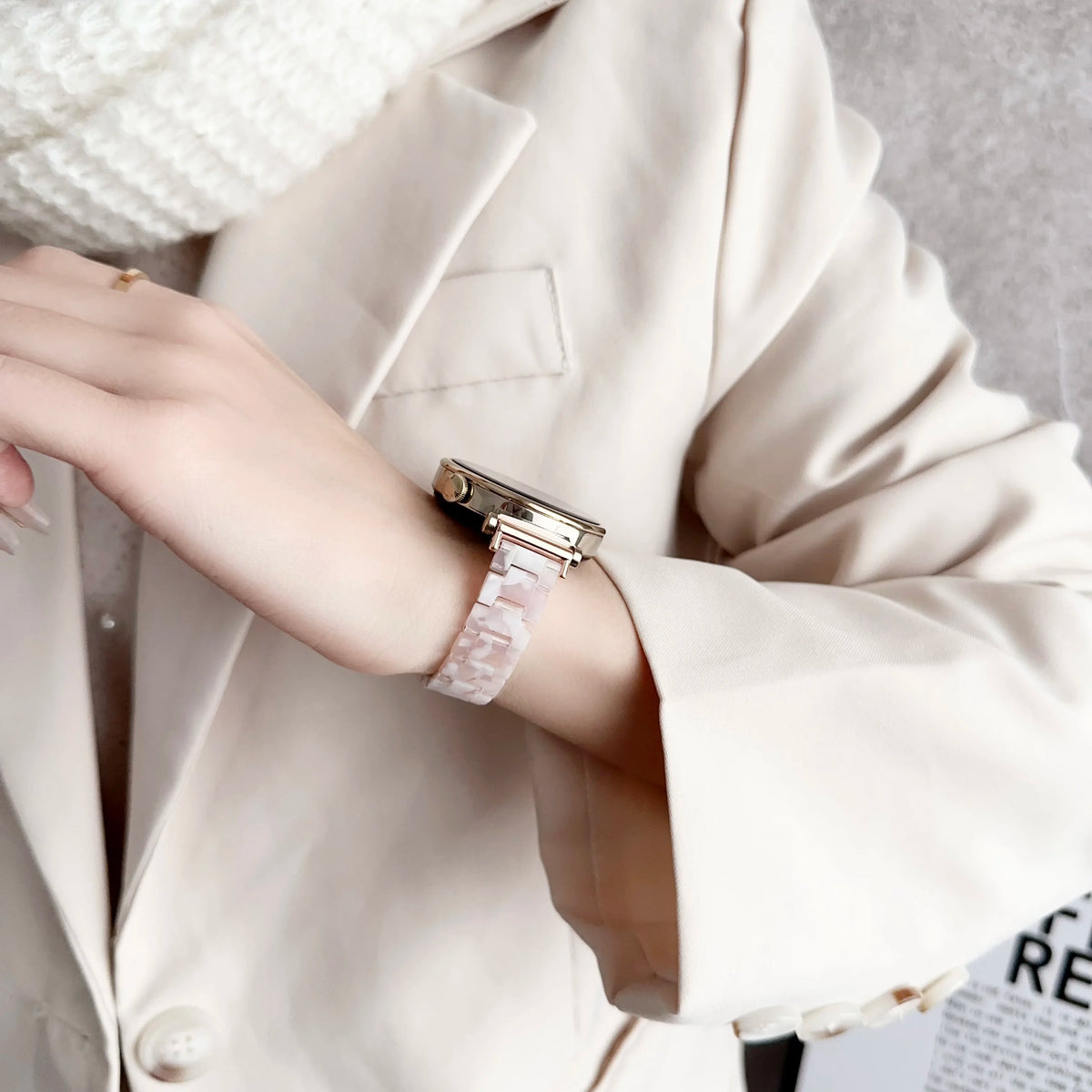 A close-up of a wrist wearing a resin beaded watch band with a three-bead design on a light blazer sleeve.