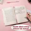 An open premium PU leather A5/A6 journal notebook with handwritten text and a pen on a pink background.