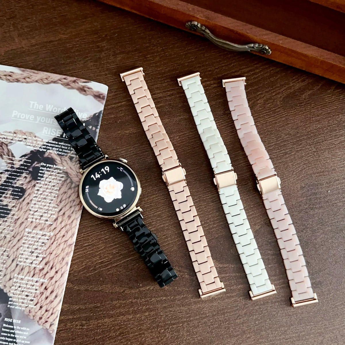 A black resin beaded watch with a gold-tone watch band is displayed next to three other watch bands.