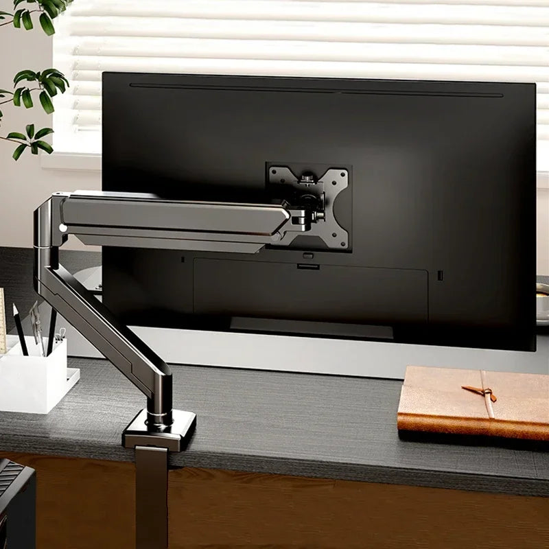 A silver adjustable monitor arm is mounted to a black computer monitor on a dark desk.