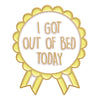 A gold-edged circular pin featuring the text I GOT OUT OF BED TODAY