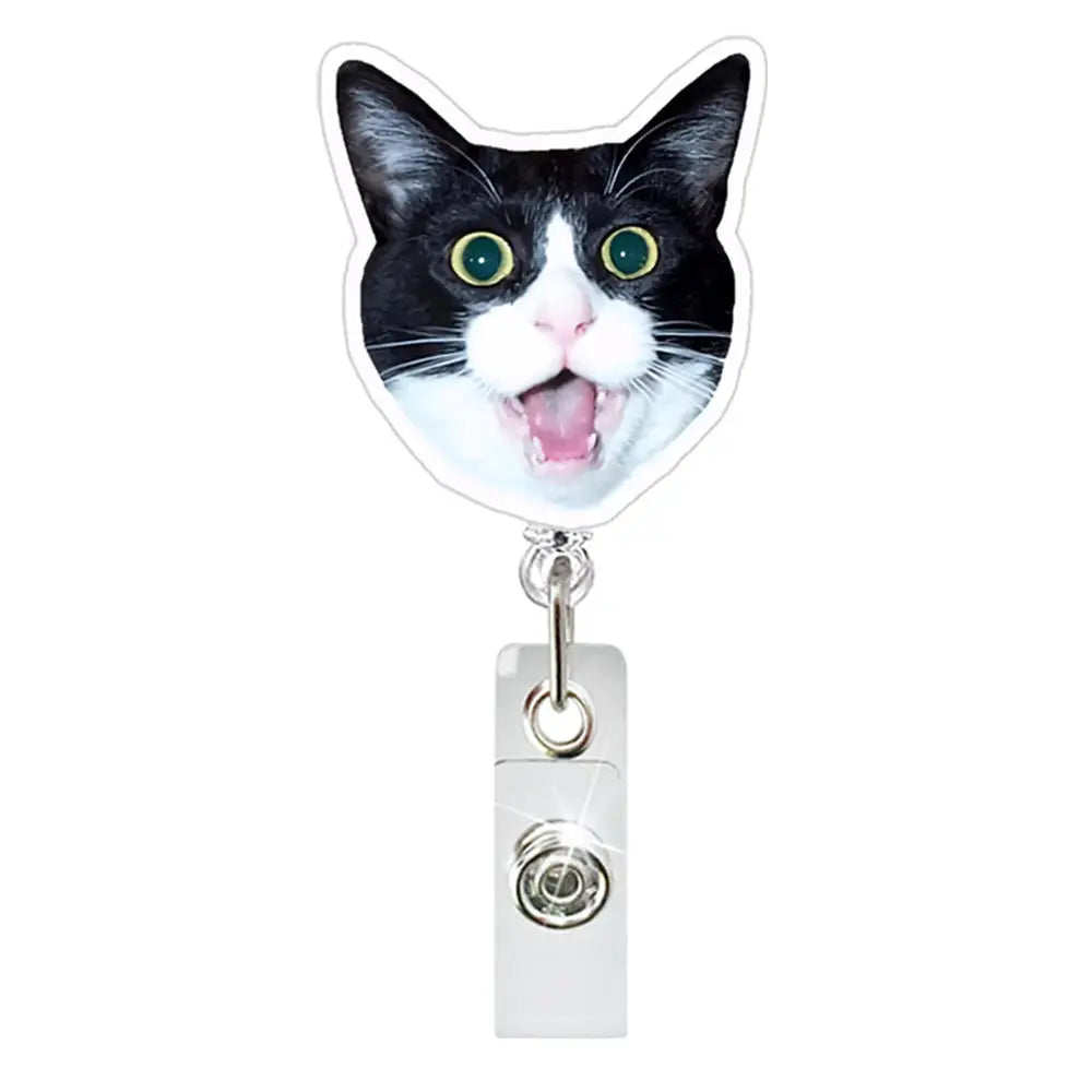 A black and white cat face charm attached to a retractable ID badge holder with a crocodile clip.