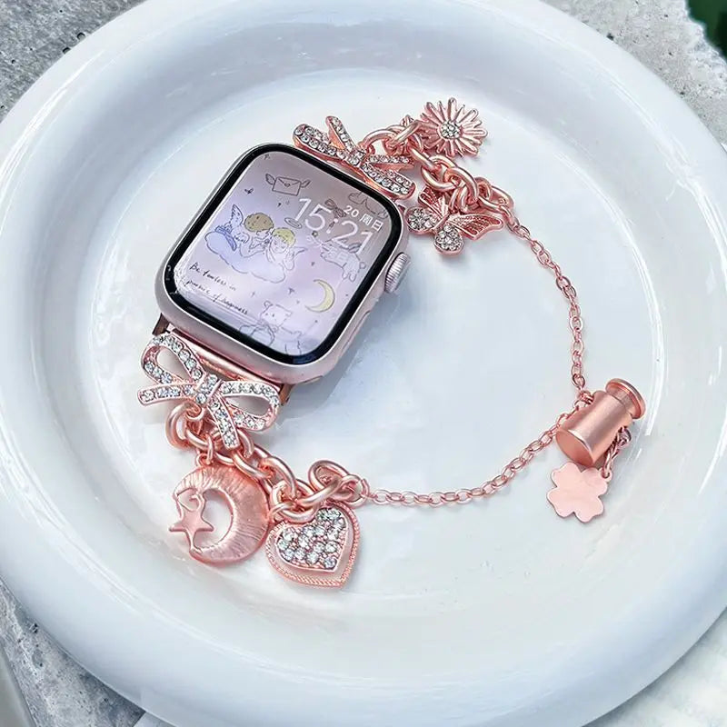 A pink diamond butterfly watch strap is displayed next to an Apple Watch on a white plate.