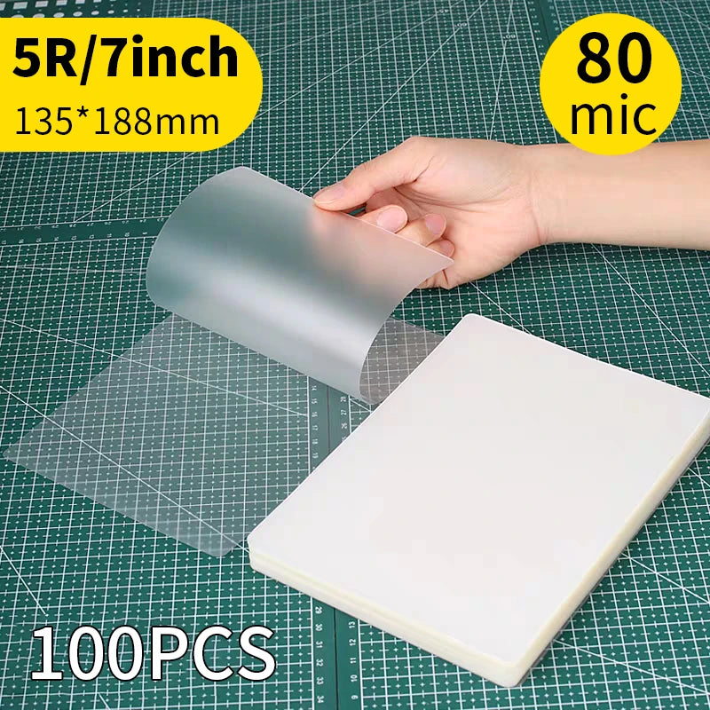 A hand holds a clear thermal laminating pouch, showing its size and material on a grid background.