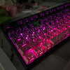 Primer plano de un teclado mecánico con teclas de gradiente rosa y púrpura vibrantes iluminadas.