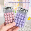 A hand holds a clear plastic mini silent calculator with a pink and purple keypad and a digital display.