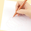 A hand holds an orange micro-pen fineliner drawing a series of concentric, wavy lines on white paper.