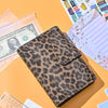 A leopard print A6 binder with a clear plastic cover is shown next to US currency and paper.