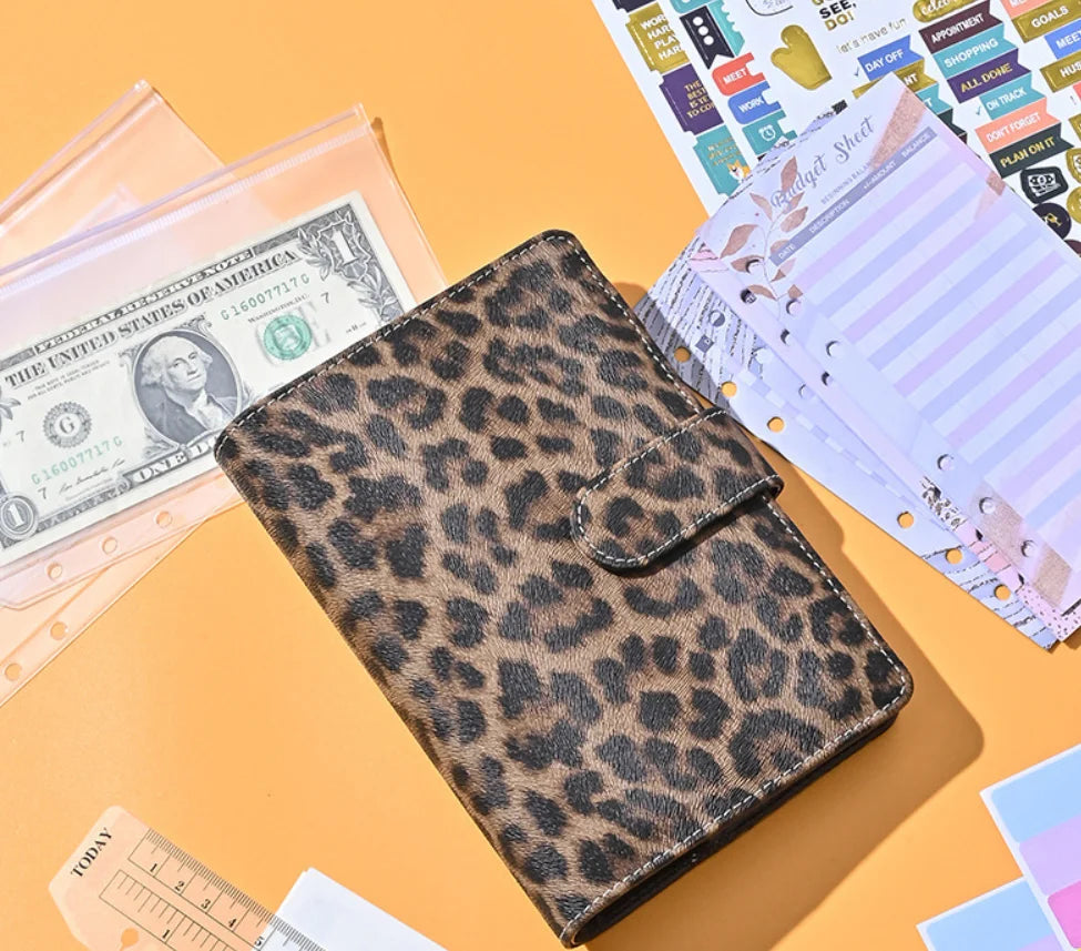 A leopard print A6 binder with a clear plastic cover is shown next to US currency and paper.