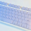 A close-up view of white custom profile keycaps for a mechanical keyboard, showing various letter and function keys.