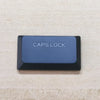 A dark blue caps lock keycap for a keyboard, labeled CAPS LOCK.