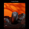 Schwarze ergonomische kabellose Gaming-Maus auf dunklen Felsen mit starken orangefarbenen Schatten.