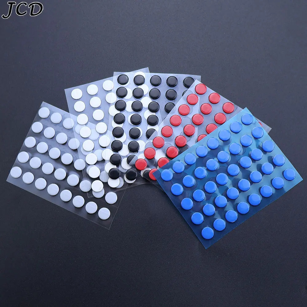 A collection of adhesive mouse skates in various colors, including black, white, red, and blue, arranged on a dark surface.