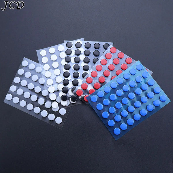 A collection of adhesive mouse skates in various colors, including black, white, red, and blue, arranged on a dark surface.