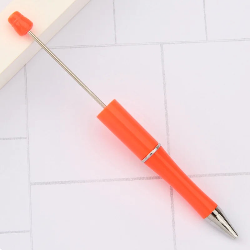 An orange DIY beadable pen with a silver tip and a plastic cap resting on a white surface.