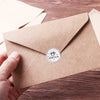 A hand holds a kraft paper envelope with a round seal that reads BONJOUR