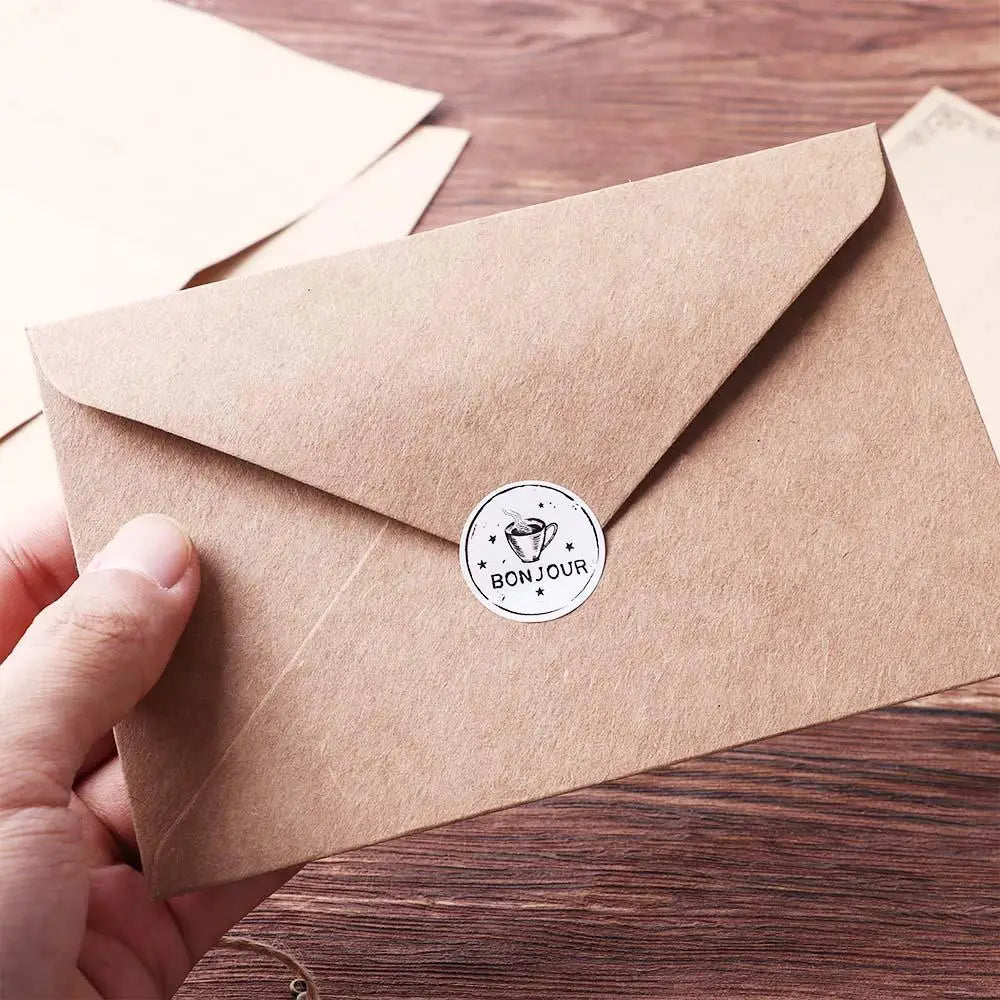 A hand holds a kraft paper envelope with a round seal that reads BONJOUR