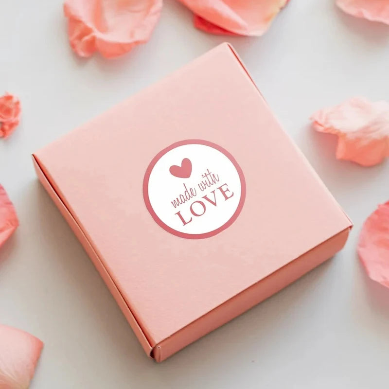 A pink box with a heart design is shown on a white surface surrounded by pink tissue paper petals.