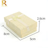 A rectangular jewelry gift box with a light beige exterior and a pale yellow ribbon, shown from above.