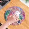 A hand is placing a white mouse on a pink disco ball shaped mouse pad with a non-slip rubber base on a wooden table.