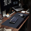 A large black non-slip gaming desk mat featuring a cute cat mouse design placed on a wooden desk with computer equipment.