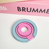 A pink and blue magnetic phone grip and stand with a foldable ring resting on a white surface.