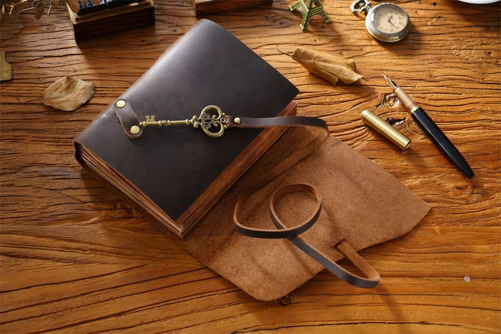 Un diario mágico de cuero hecho a mano abierto sobre una mesa de madera con llaves antiguas y una correa de cuero cercana.