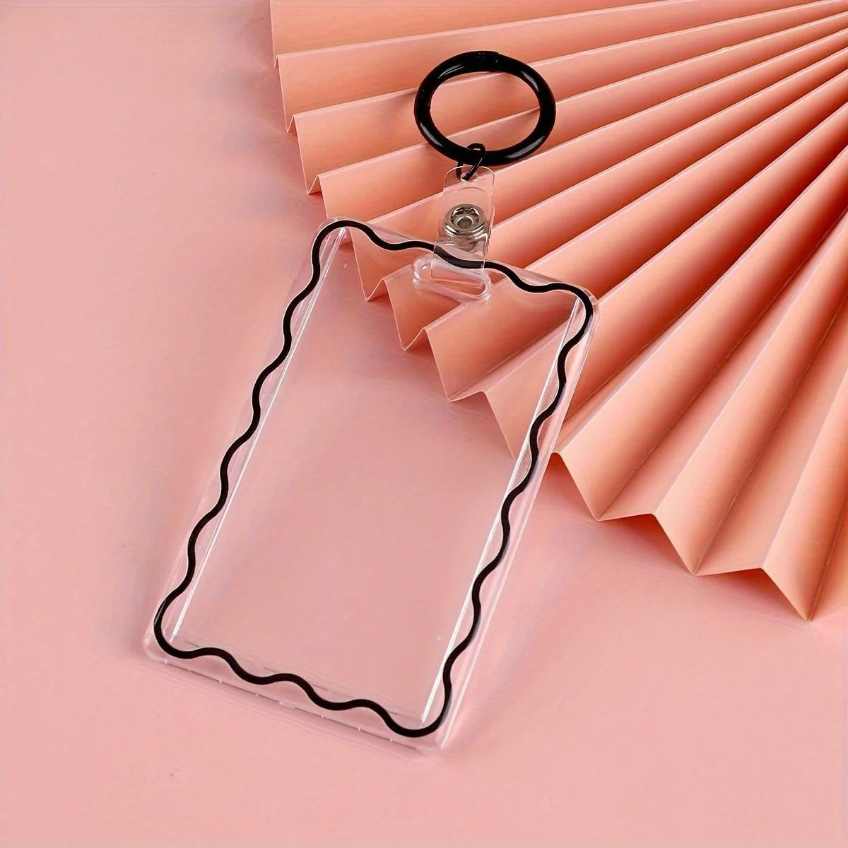 Clear acrylic card holder with a black decorative border and attached to a key ring, set against a pink background.