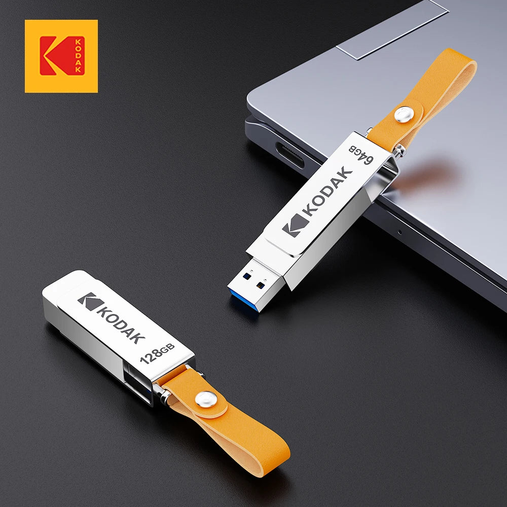 A silver Kodak metal USB flash drive with a leather orange lanyard is shown next to a laptop.