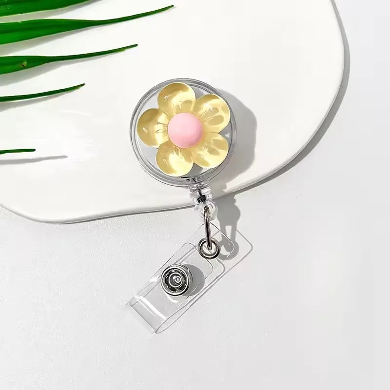 A clear retractable ID badge holder featuring a floral pull buckle with yellow and pink accents.