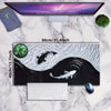 A gaming mouse pad featuring a black and white koi pattern, displayed next to a monitor and a green succulent.