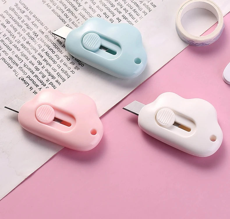 Two portable utility knives in light blue and pink are shown resting on a piece of paper.
