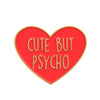 A red heart-shaped enamel pin with the text CUTE BUT PSYCHO in gold lettering.