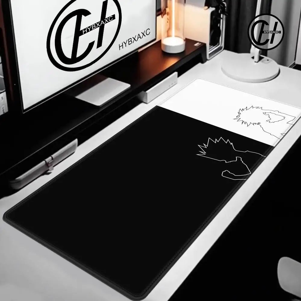 A black extra large gaming mouse pad is displayed on a white desk next to a monitor and a desk lamp.
