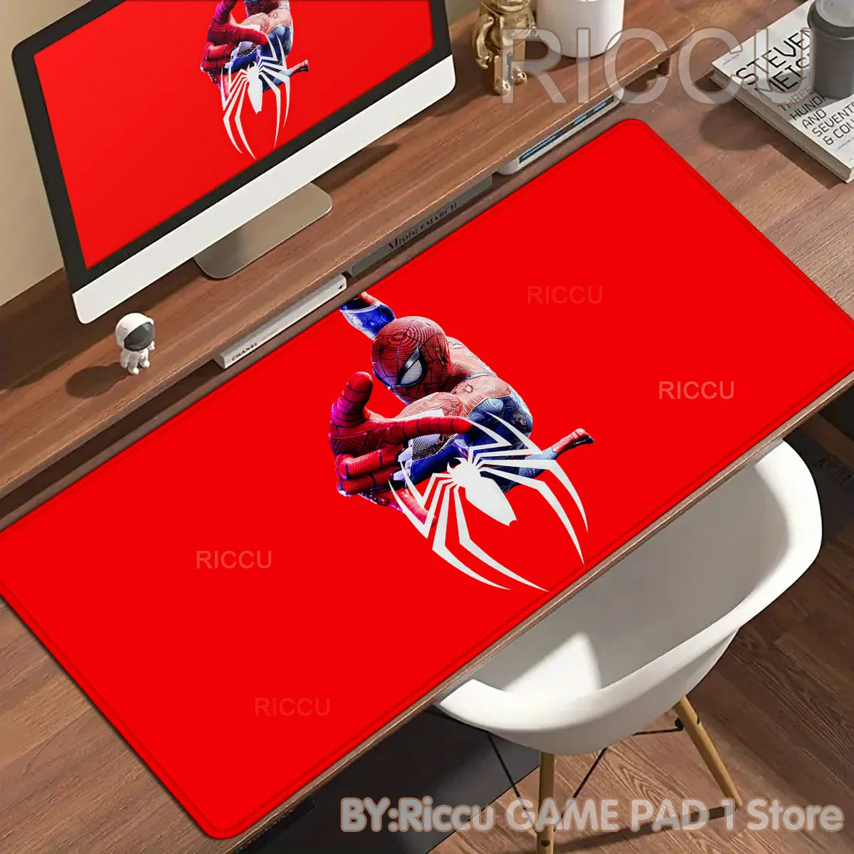 A red desk mat featuring a Spider-Man design placed on a wooden desk next to a computer monitor.