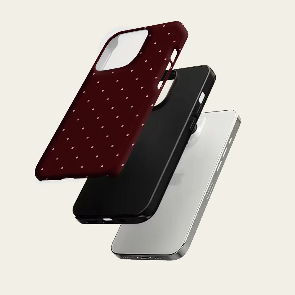 Una funda de teléfono roja oscura con lunares junto a una funda transparente sobre un fondo gris claro.