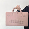 A pink laptop sleeve with a handle is held by a person against a white background.