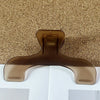 A close-up of a bronze book page clip with a curved shape resting on a white surface.