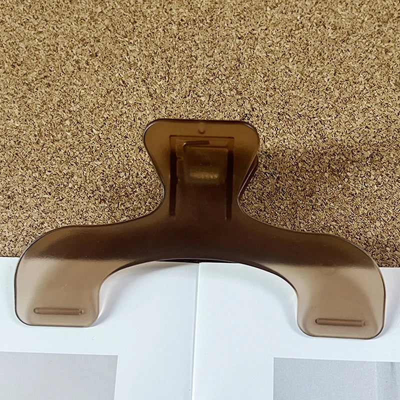 A close-up of a bronze book page clip with a curved shape resting on a white surface.