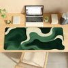 A dark green and cream abstract wave mouse pad placed on a wooden desk next to a laptop.