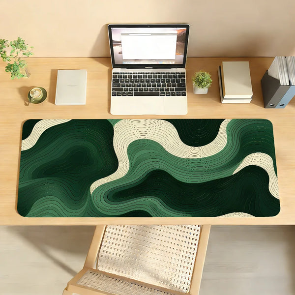 A dark green and cream abstract wave mouse pad placed on a wooden desk next to a laptop.