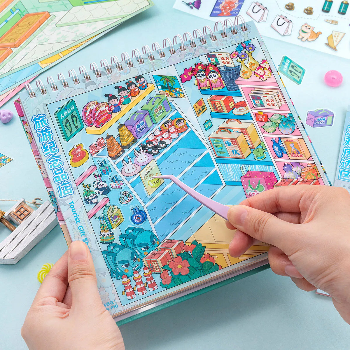 A hand holds an open sticker book featuring a cute snack shop scene with various food items and colorful decorations.