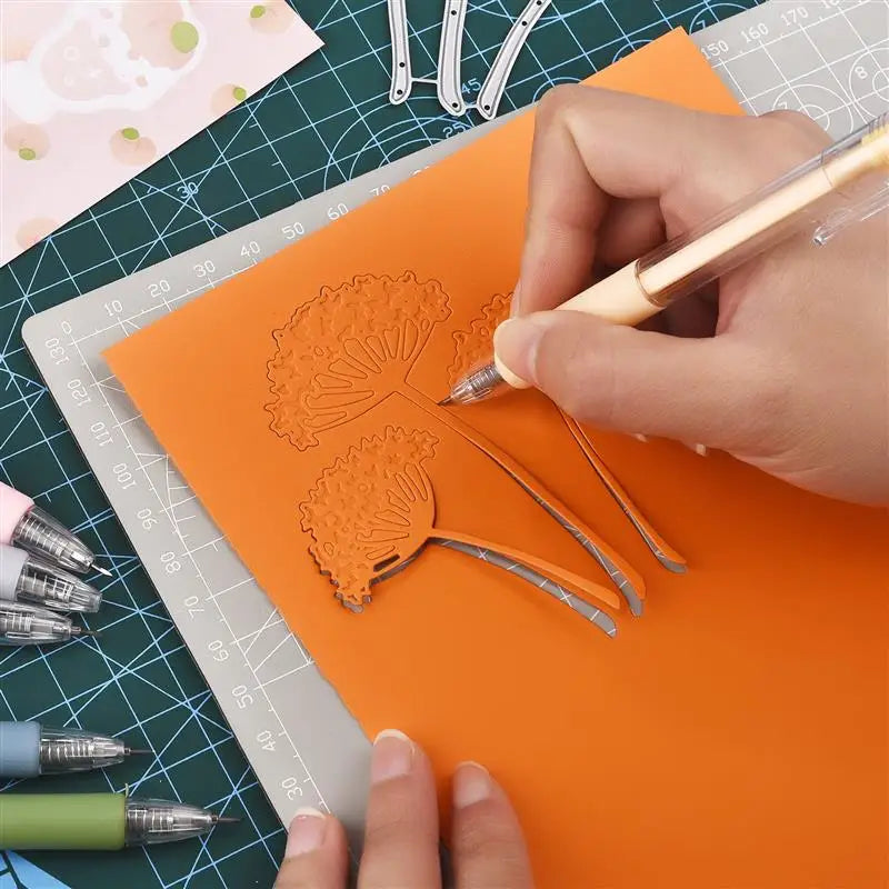 A hand uses a precision utility knife to cut intricate orange paper designs on an orange sheet within a crafting context.